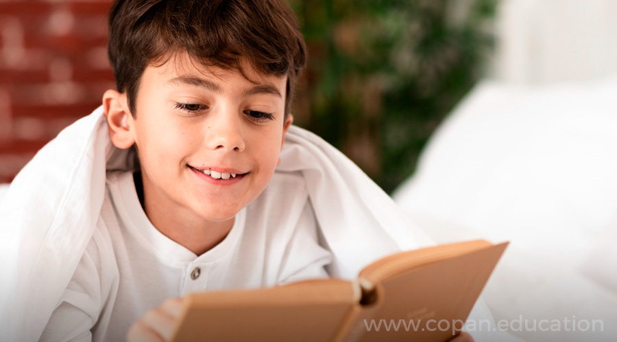 Niño pequeño sonriente que lee en casa